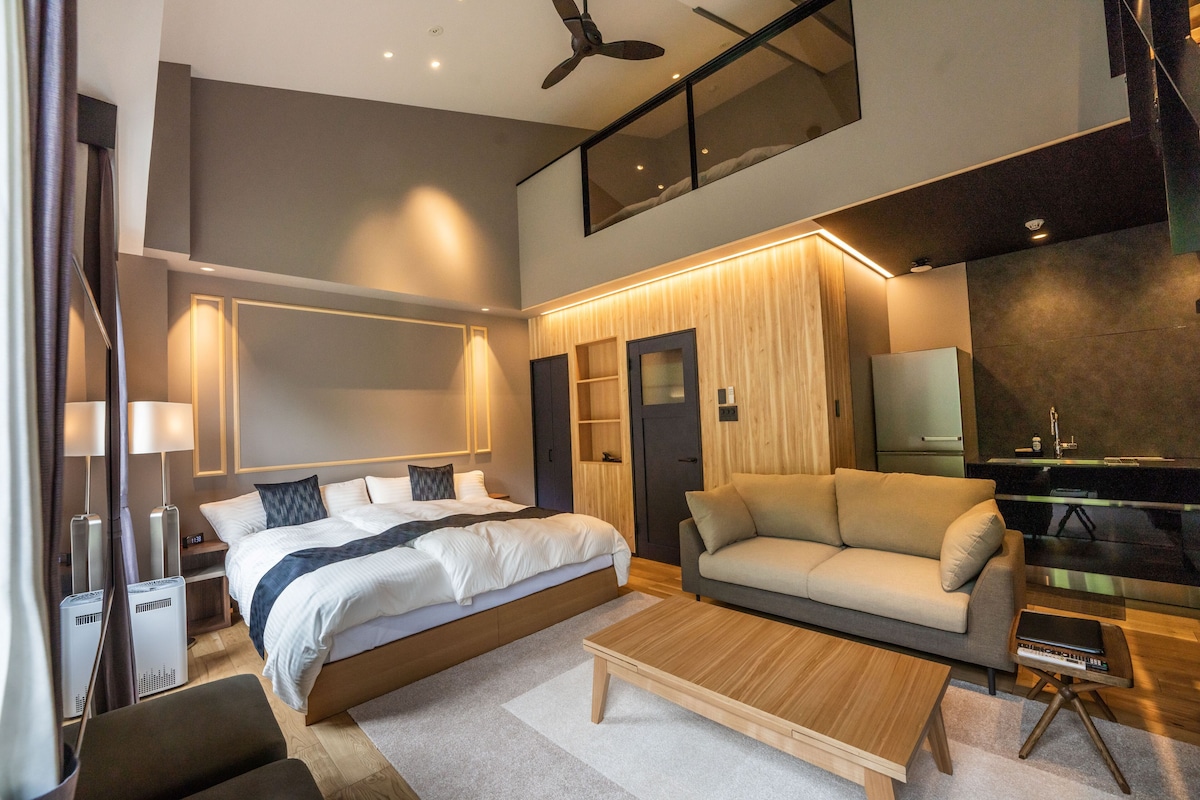 A modern hotel room with a large bed, a sofa, a coffee table, and a TV.