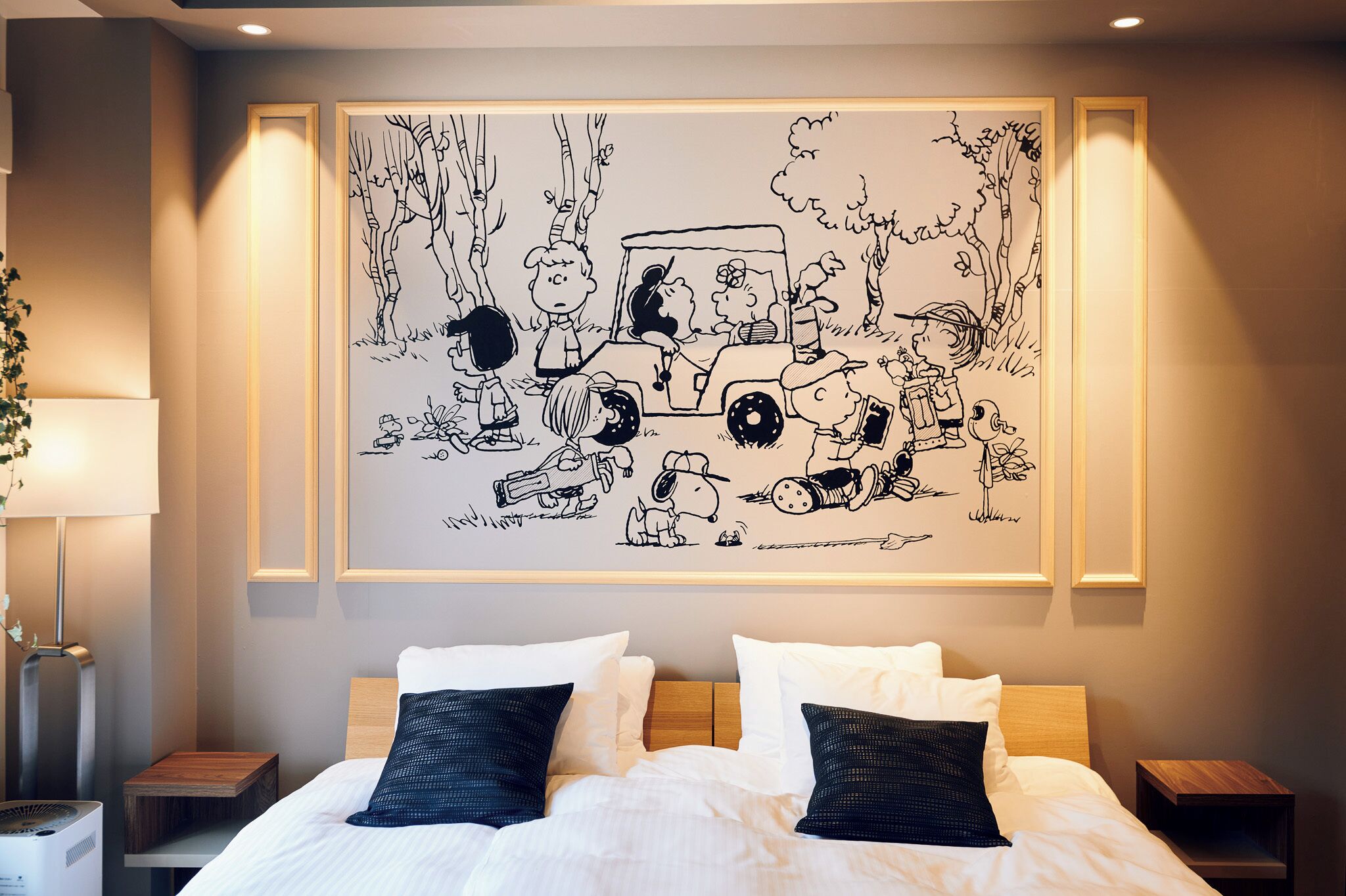 A bedroom with a large wall mural, a bed with white linens, two bedside tables, and a lamp.