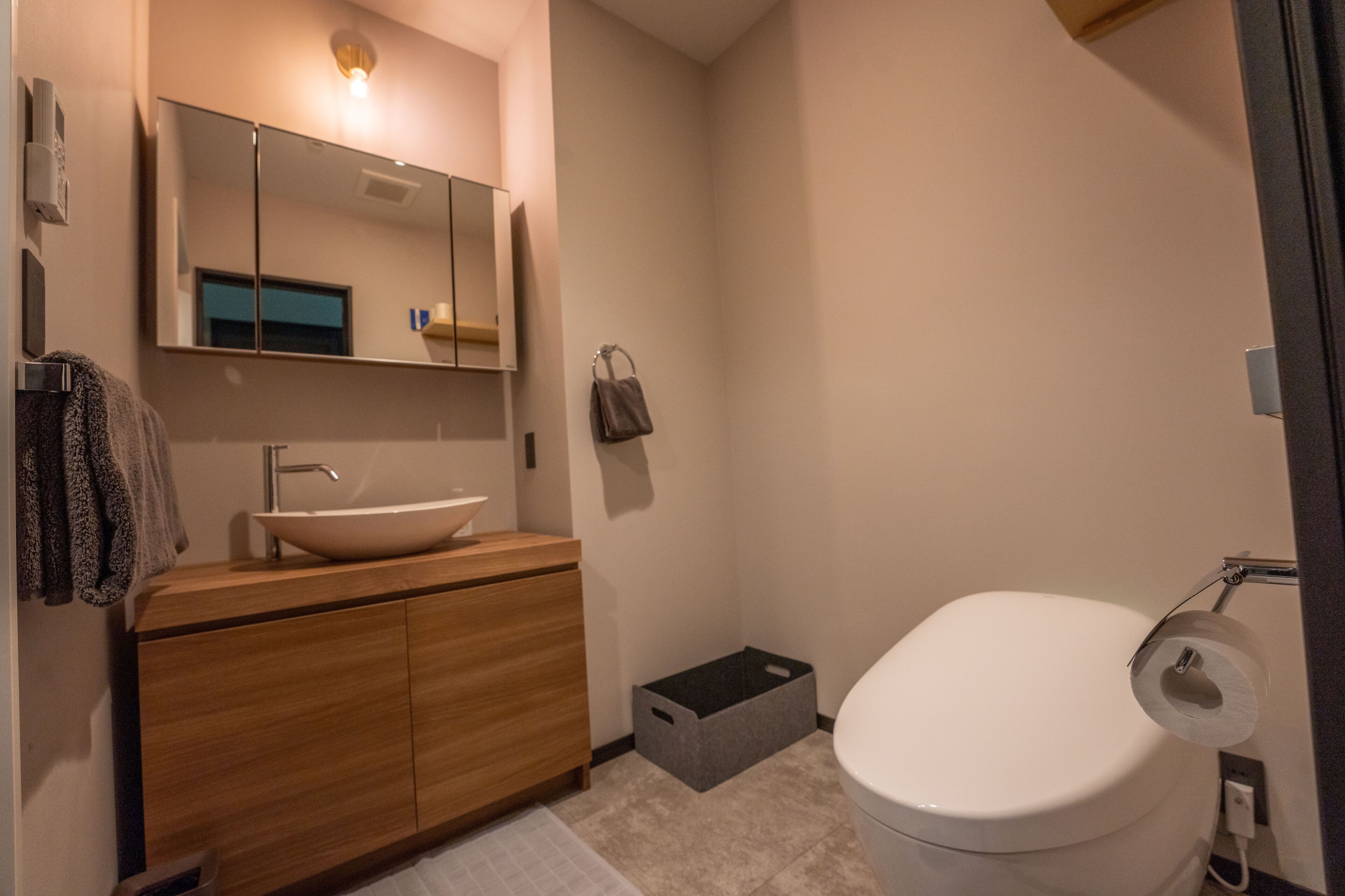 A modern bathroom with a wooden vanity, a large mirror, a white sink, and a toilet.