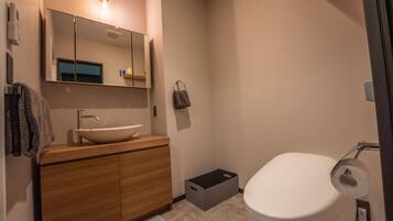 A modern bathroom with a wooden vanity, a large mirror, a white sink, and a toilet.