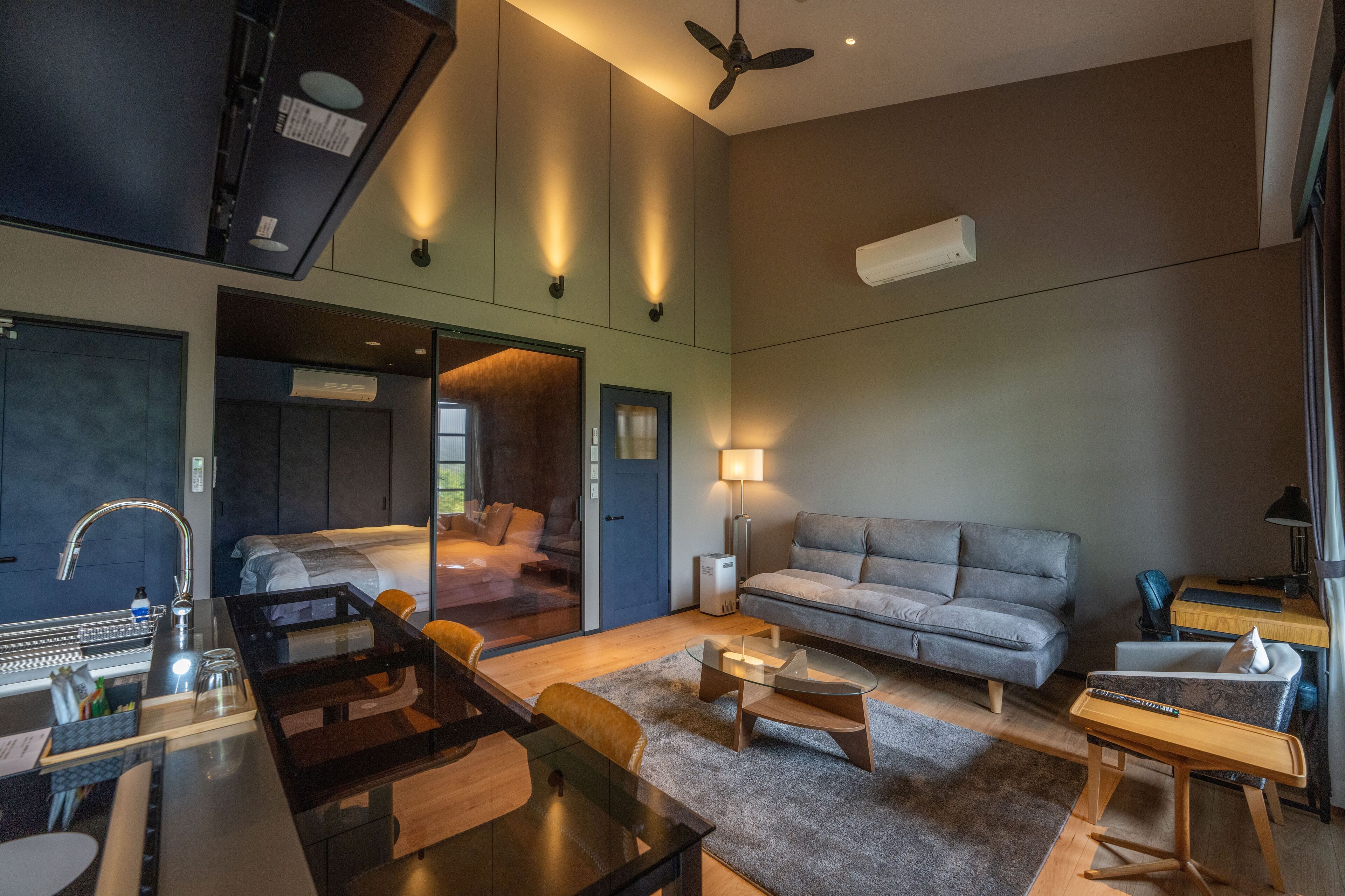 Una habitación de hotel moderna con zona de comedor, sofá, mesita y ventilador de techo.