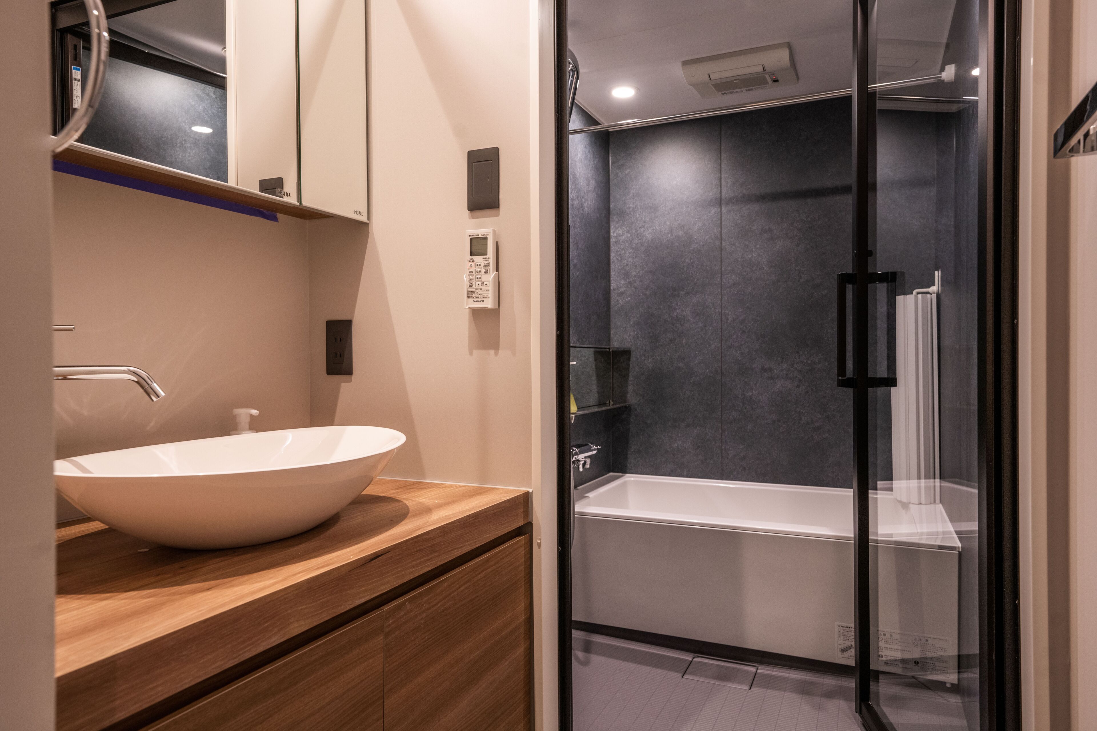 Un baño moderno con un lavamanos grande blanco, tocador de madera y zona de ducha con mampara de vidrio.