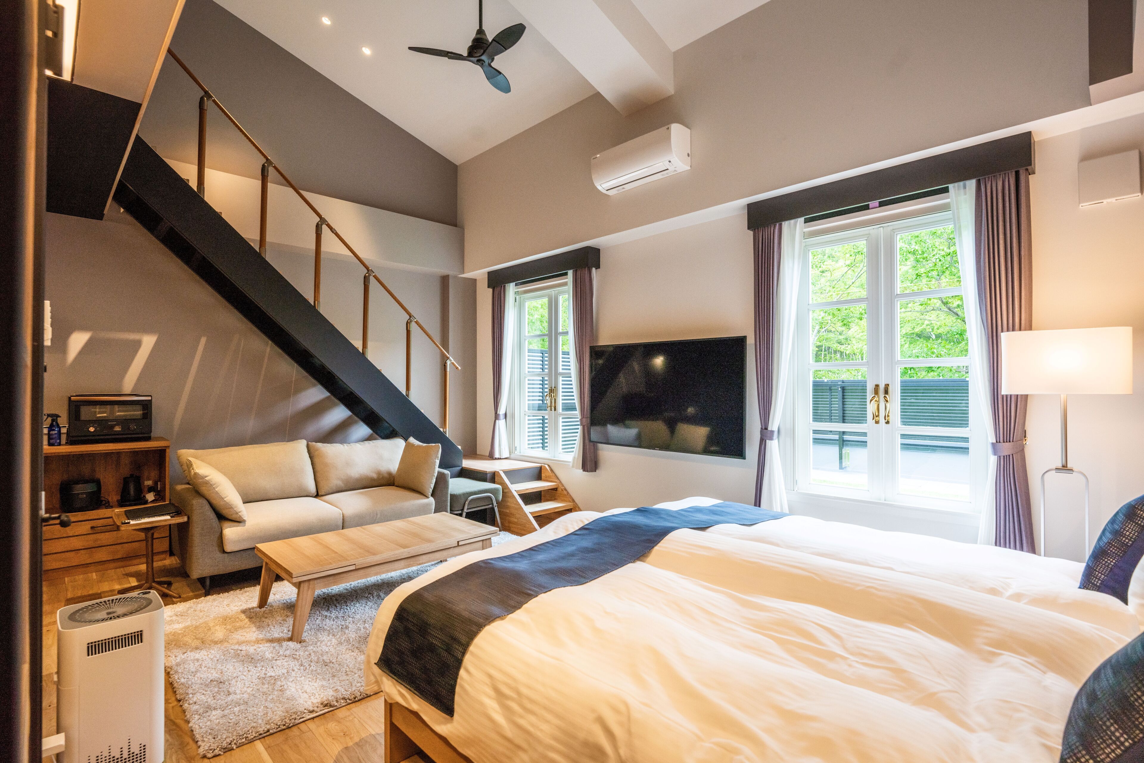 A modern bedroom with a bed, a sofa, a desk, and a staircase.