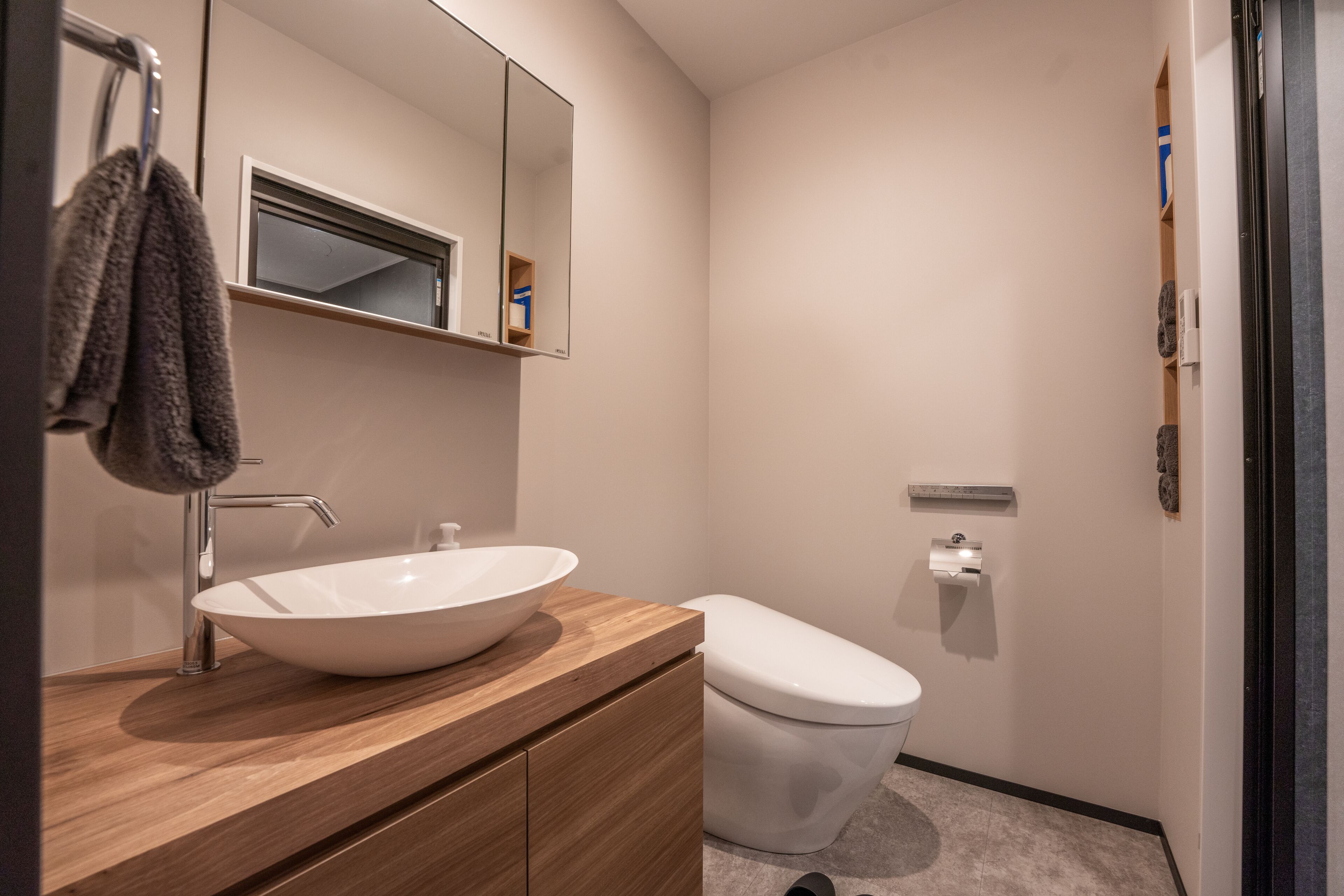A modern bathroom with a wooden vanity, a white sink, a toilet, and a towel hanging on a rack.