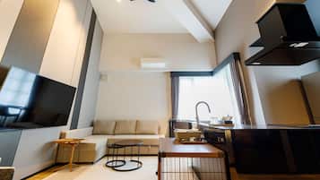 Una sala moderna con televisión de pantalla plana, un sofá, una mesa de centro y una zona de cocina con fregadero y estufa.