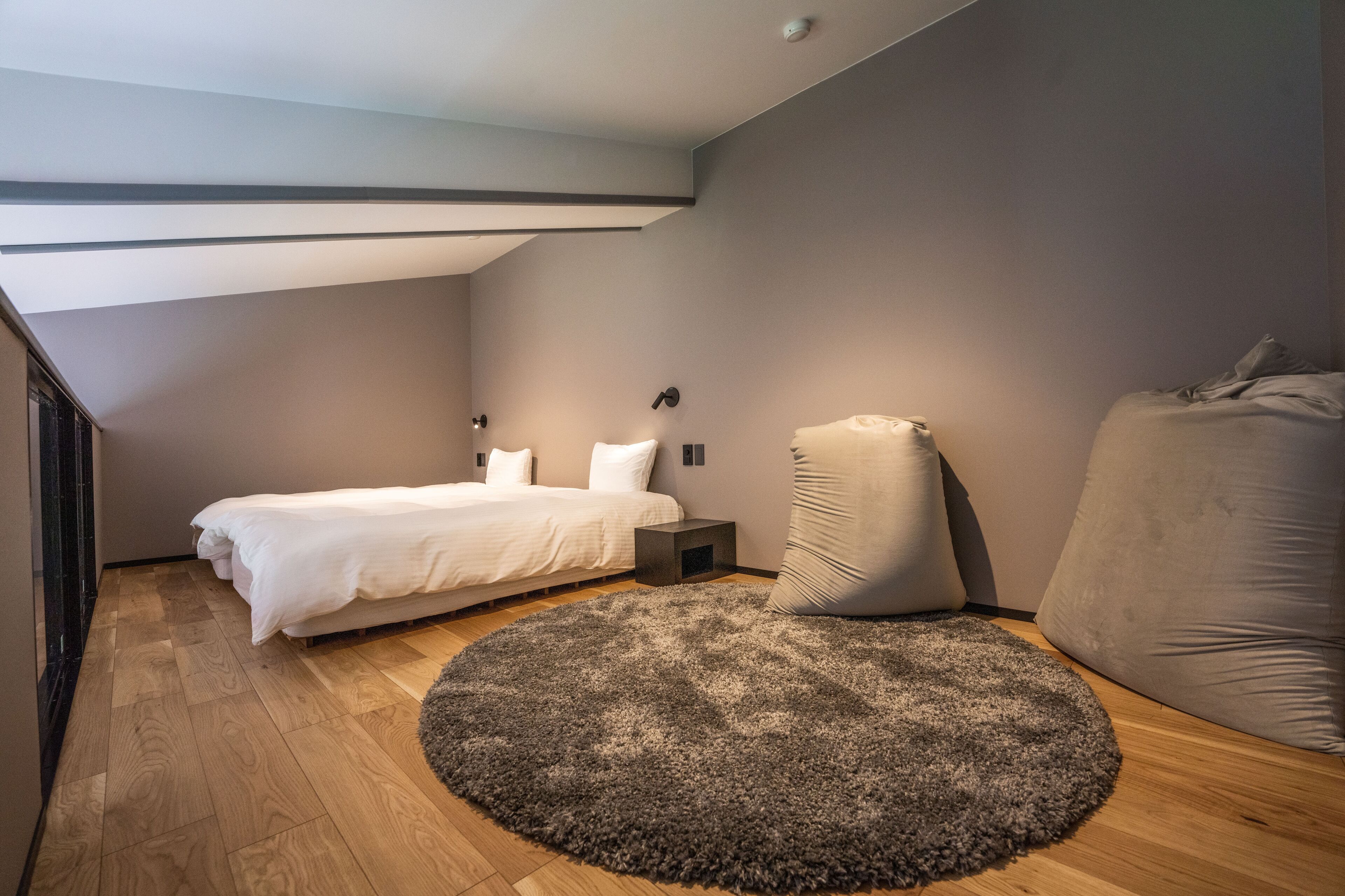 Un dormitorio con cama, un tapete redondo, una mesita de noche y un almohadón grande.