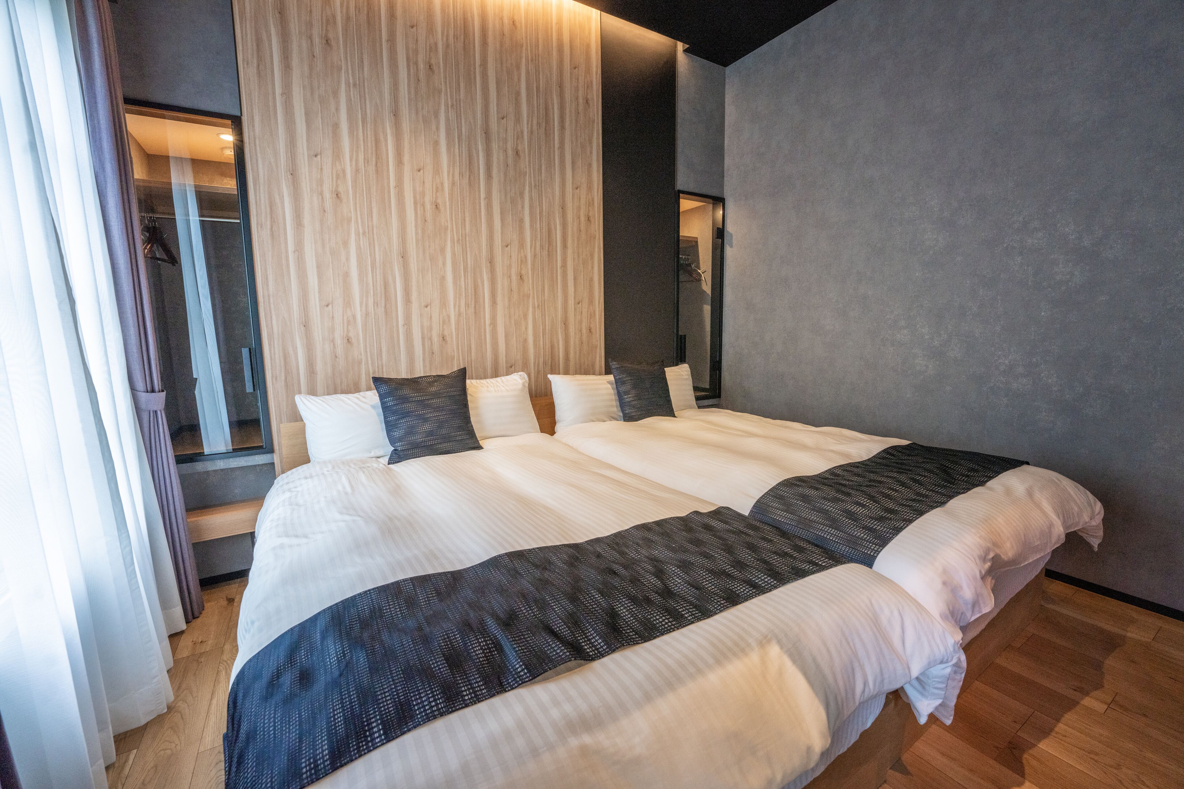 A double bed with white and dark gray linens, a wooden headboard, and a gray wall.