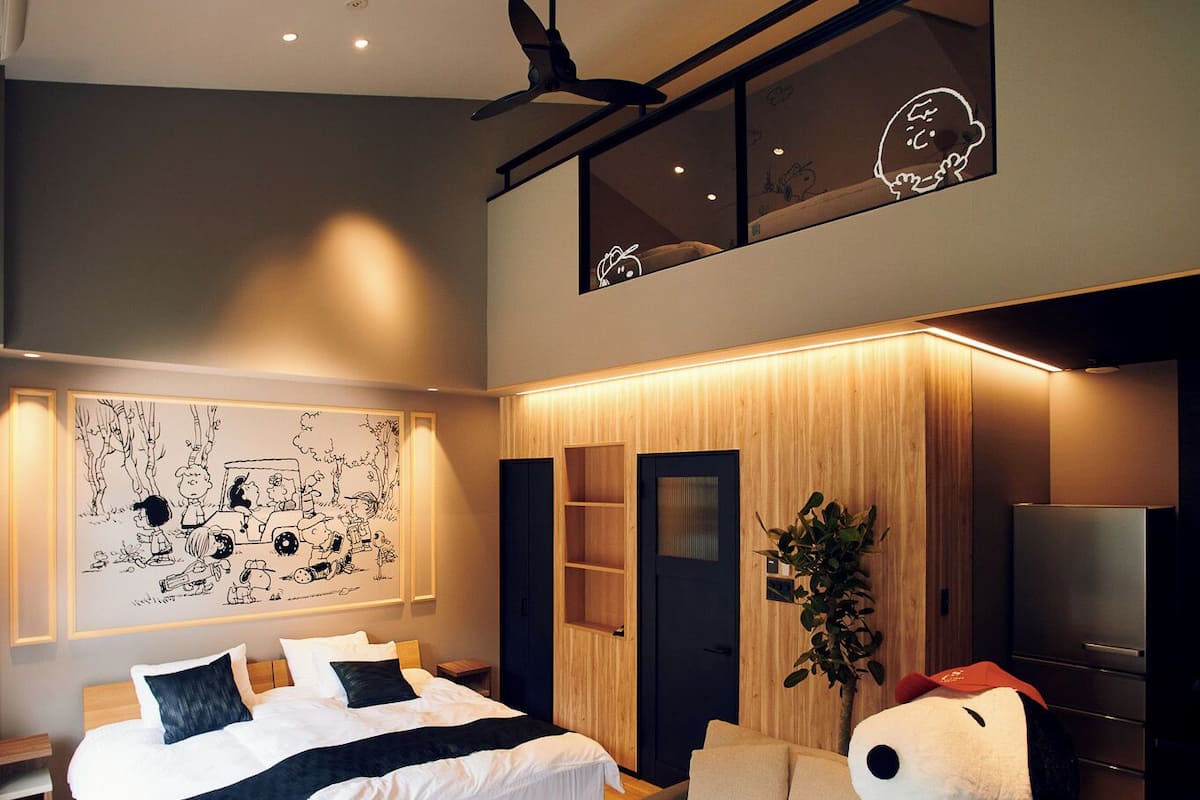 Une chambre à coucher moderne avec un lit, un canapé, un grand ours en peluche, un ventilateur de plafond et un téléviseur.