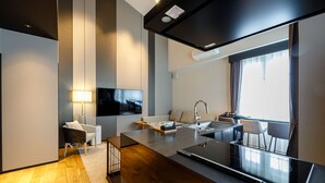 A modern kitchen with a large island, a built-in oven, and a sink. There is a flat-screen TV mounted on the wall, a sofa, and a dining area with chairs. - eau sol vert karuizawa club (Karuizawa)