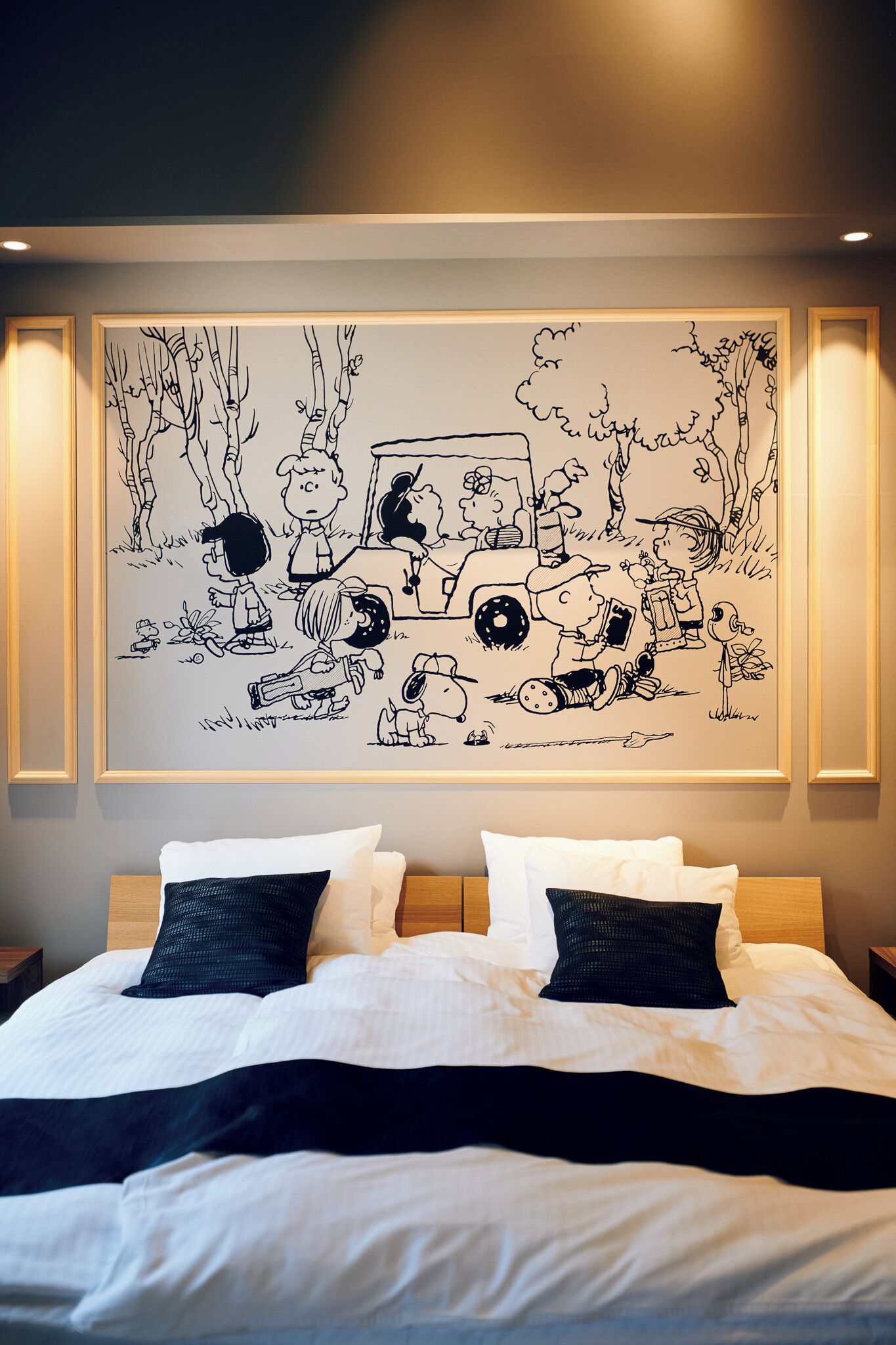 Una camera da letto con un letto grande, due cuscini e un'opera d'arte appesa al muro raffigurante una scena con un'auto e dei personaggi.