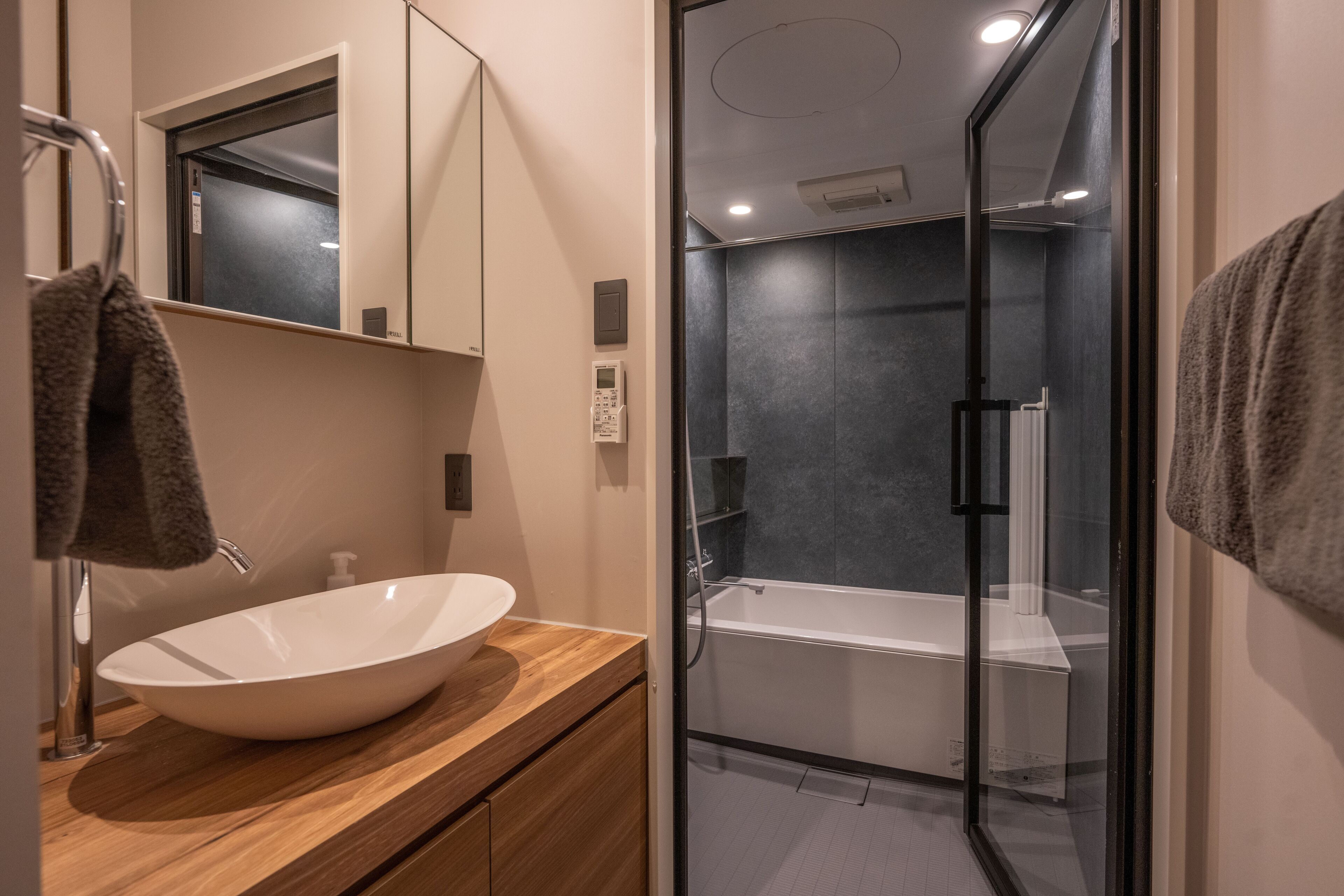 A modern bathroom with a large white vessel sink, a glass-enclosed shower, and a wooden vanity.
