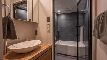 A modern bathroom with a large white vessel sink, a glass-enclosed shower, and a wooden vanity.