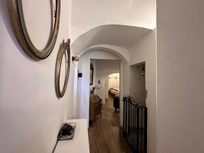A hallway with a white wall, two large mirrors, a white table with a black bag, and a wooden floor.
