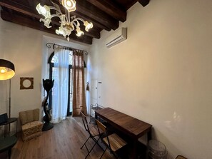 A room with a wooden dining table, a chandelier, and a large window with curtains.