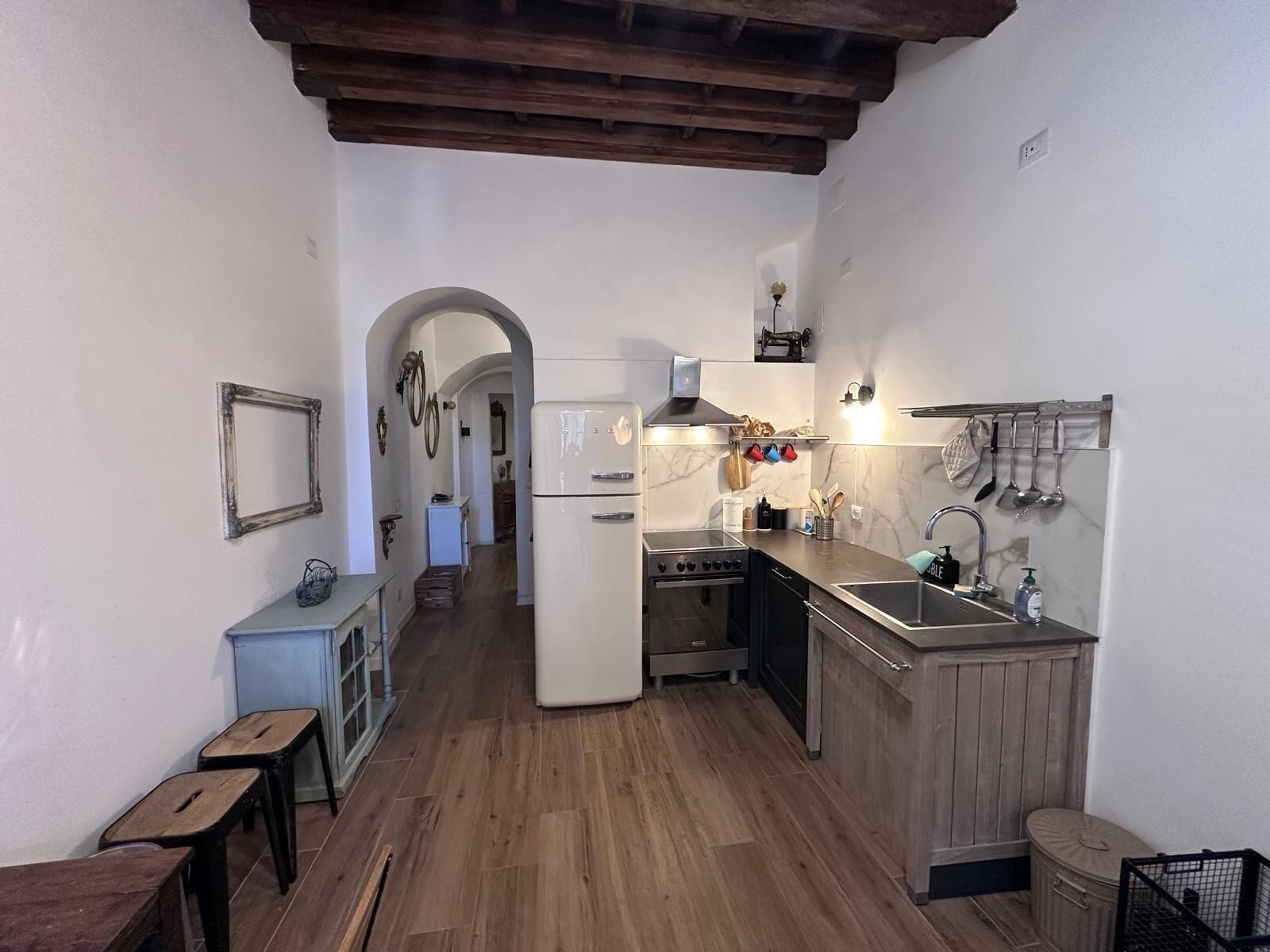 A compact kitchen with a central island, wooden flooring, and a rustic ceiling.