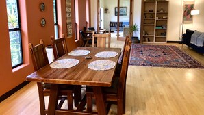 A dining area with a wooden table and chairs, a patterned rug, and a bookshelf in the background.