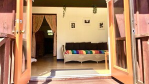 A wooden door leading into a room with a wicker sofa, a small table, and a wall-mounted plant.