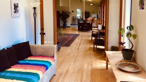 A spacious room with a wooden floor, a colorful striped bed, a dining area with chairs and a table, and a potted plant.