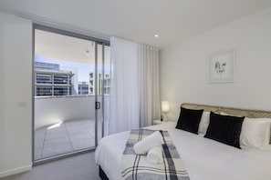 Relax in this inviting room with a large bed, sliding glass door to a balcony, and a bedside table with a lamp.