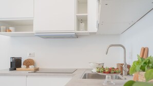 Eine moderne Küche mit weißen Schränken, einer Edelstahl-Spüle, einer Kaffeemaschine und einer Schale Erdbeeren.