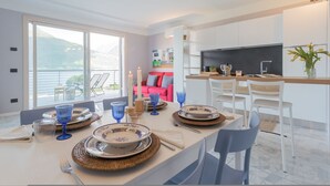 Un comedor moderno con una gran mesa lista para cuatro personas, zona de cocina y balcón con vistas a las montañas.