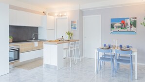 A modern kitchen with white cabinets, a central island, and a dining area with blue chairs and a white table. - Misultin House Swimming Pool (Pianello del Lario)