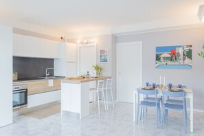 Een moderne keuken met witte kastjes, een centraal eiland en een eethoek met blauwe stoelen en een witte tafel.