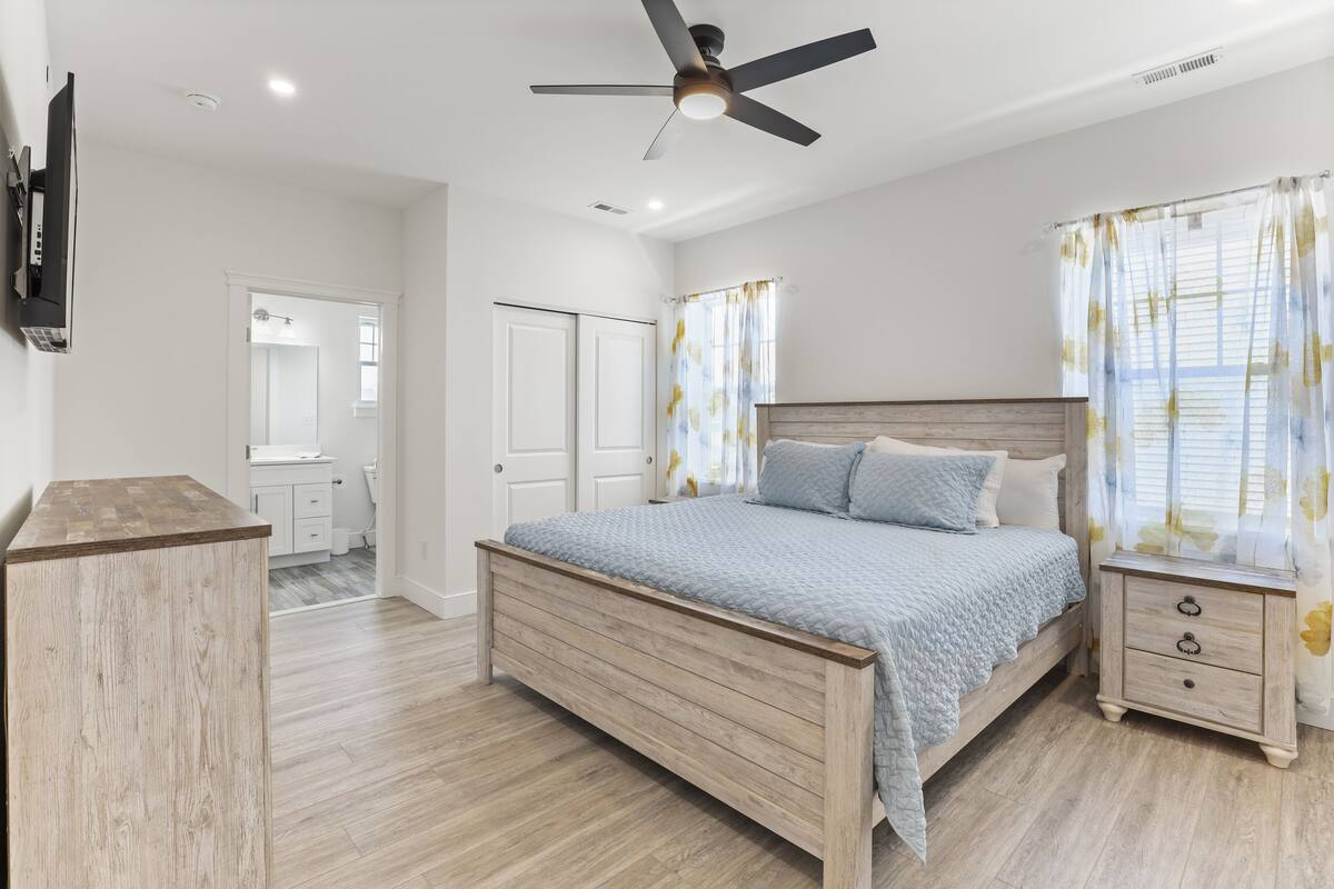 A bedroom with a wooden bed, a nightstand, a ceiling fan, and a TV mounted on the wall.