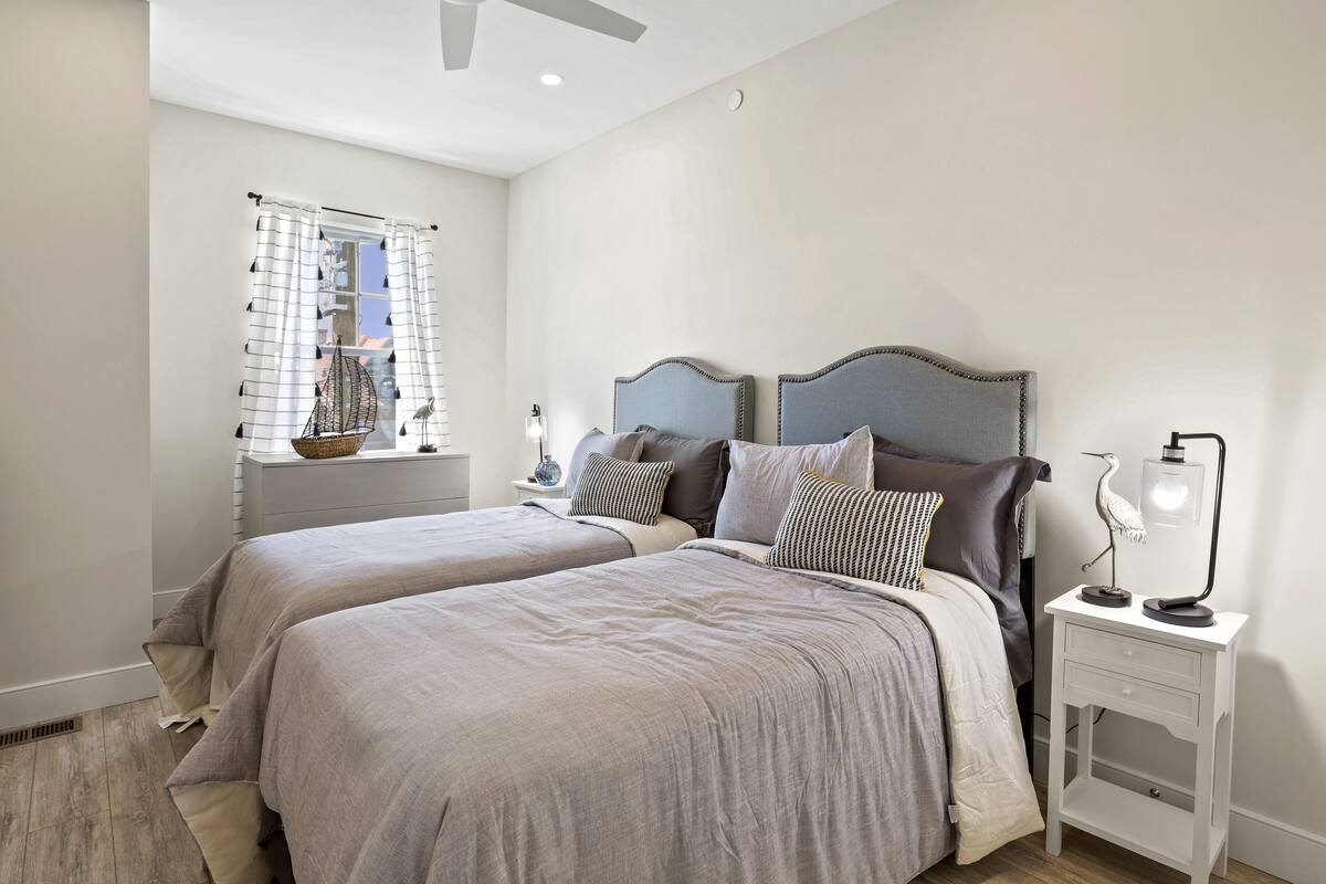 A bedroom with two beds, a nightstand, a lamp, and a window with curtains.