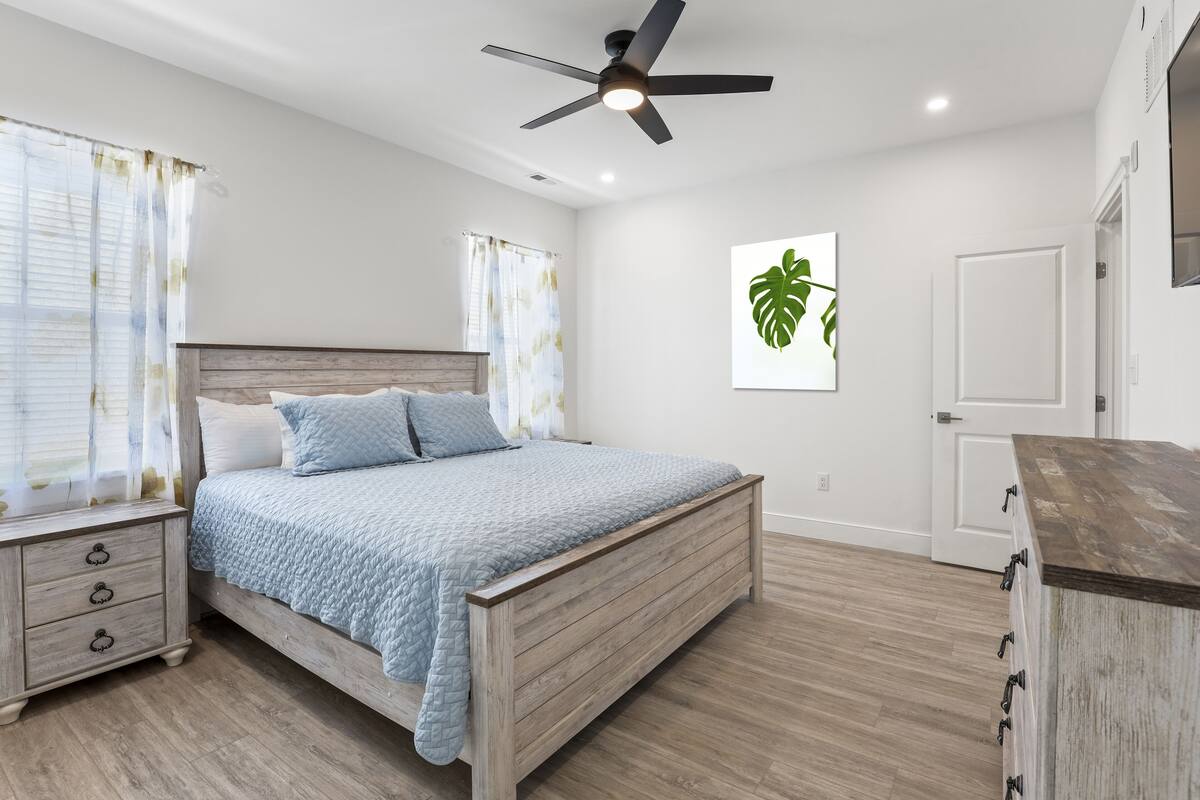 A bedroom with a bed, nightstand, ceiling fan, and a door.
