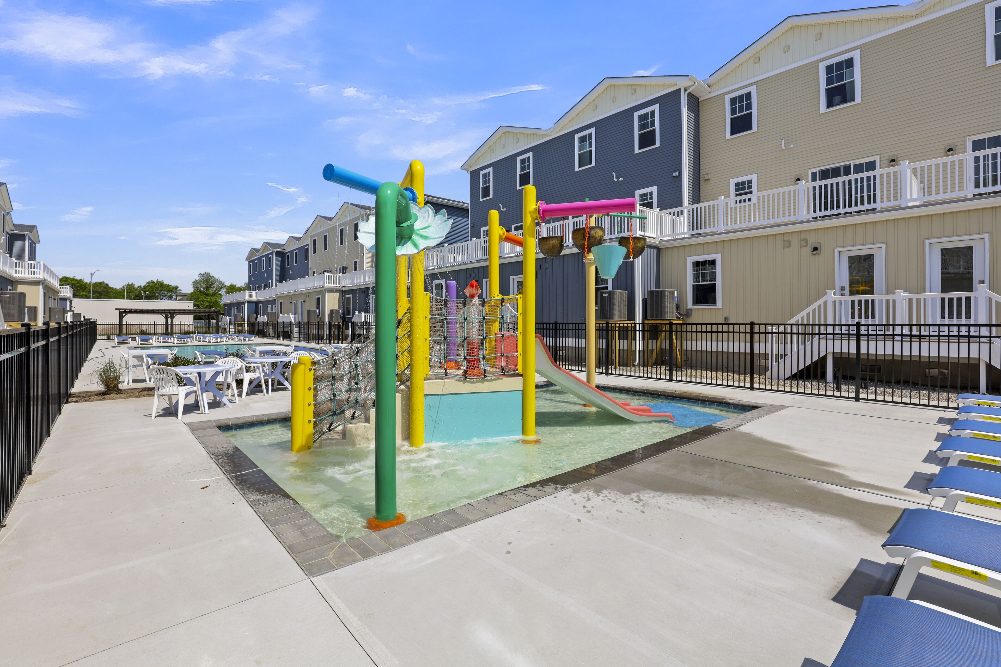 Un parque infantil con toboganes y estructuras para escalar, una piscina y sillones de descanso.