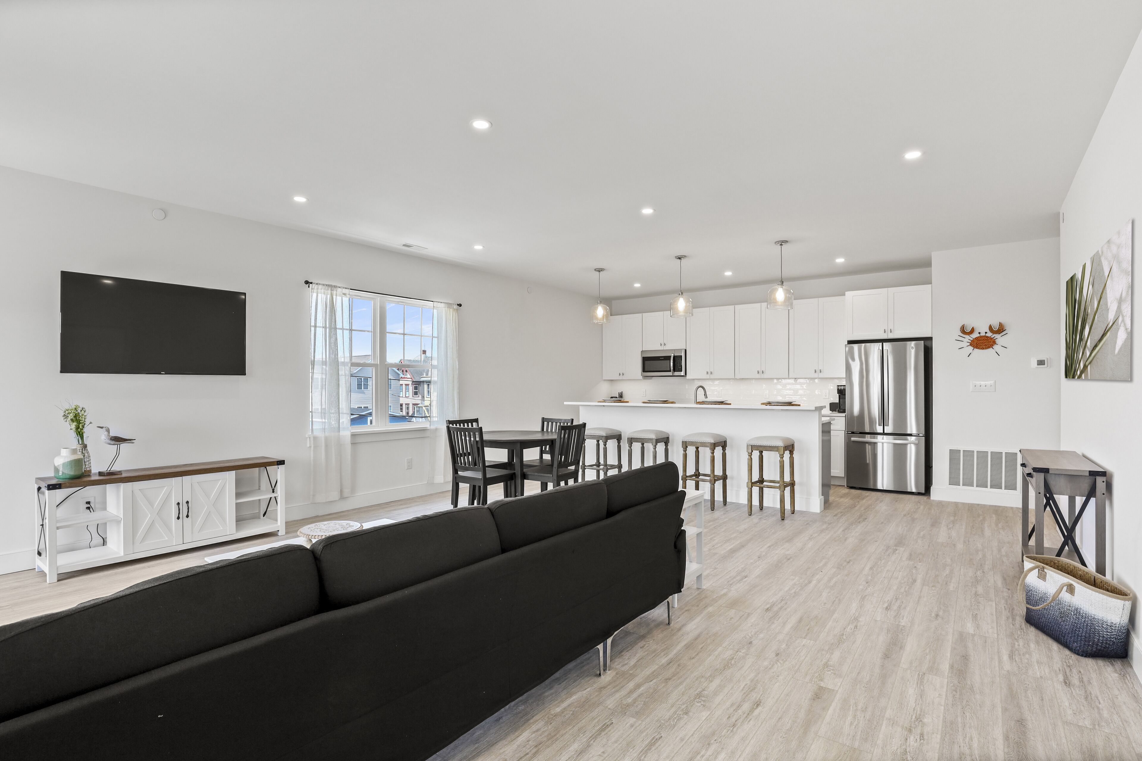 A modern kitchen with white cabinets, a stainless steel refrigerator, and a flat-screen TV mounted on the wall.