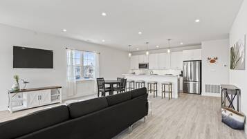 A modern kitchen with white cabinets, a stainless steel refrigerator, and a flat-screen TV mounted on the wall.