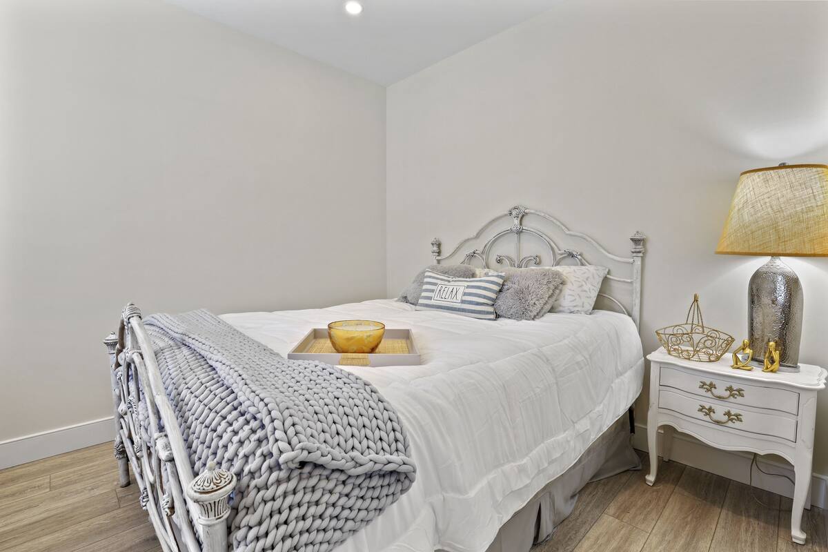 A neatly made bed with a white comforter, a gray knitted throw, and a tray with a bowl and a candle.