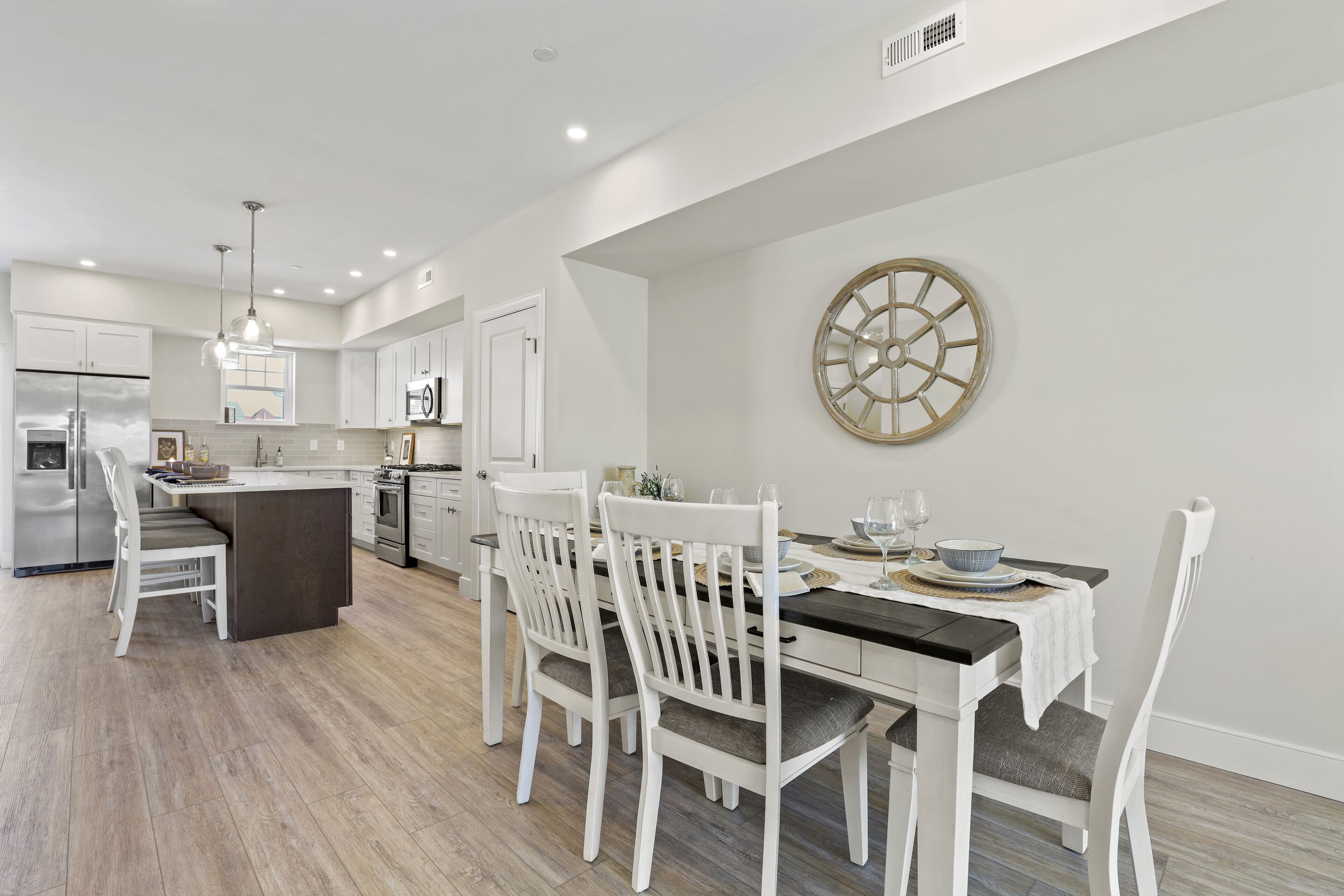 A modern kitchen with white cabinetry, a central island, and a dining area with white chairs.
