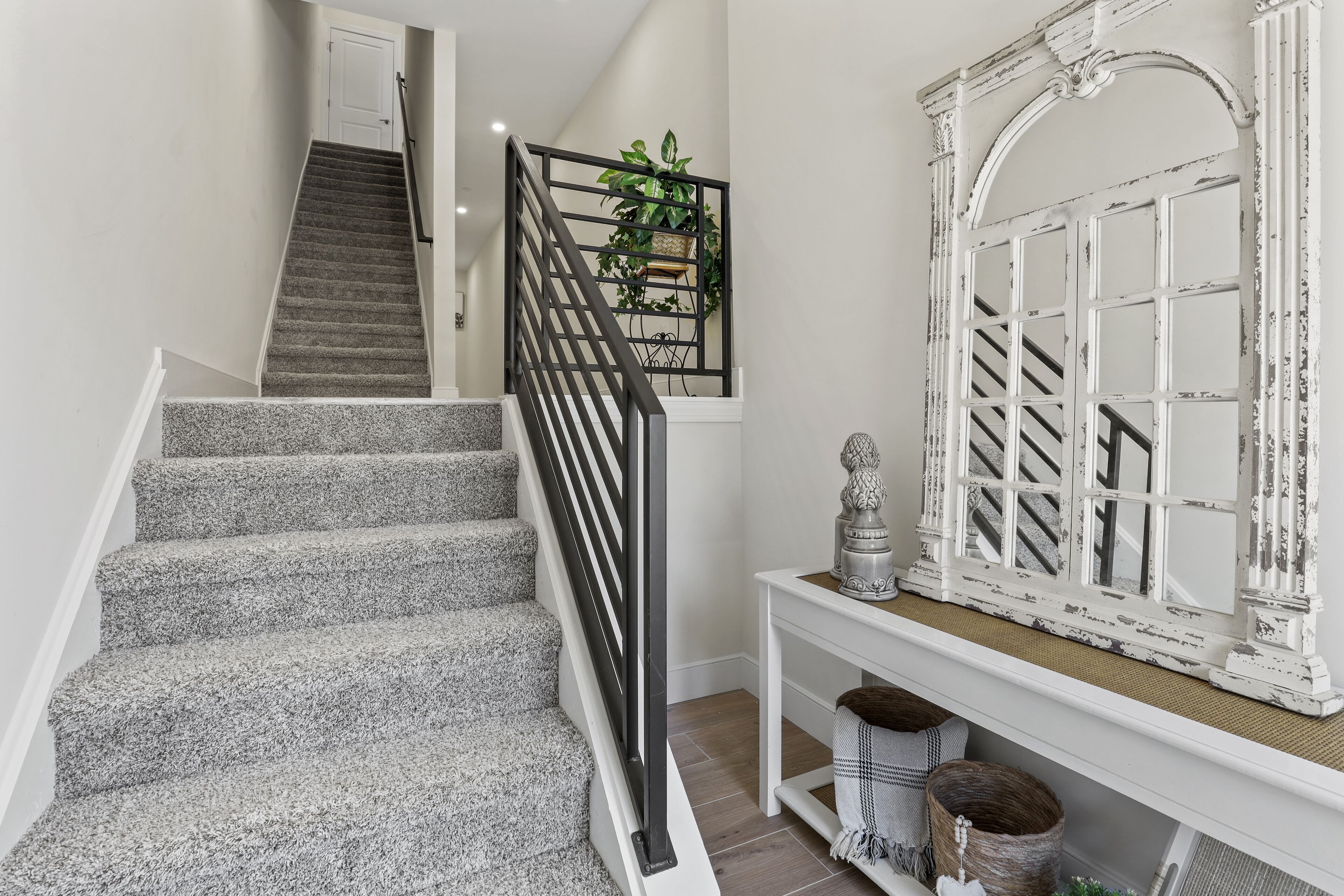 A staircase with a black railing, a white console table with decorative items, and a white-framed mirror.