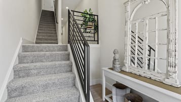 A staircase with a black railing, a white console table with decorative items, and a white-framed mirror.