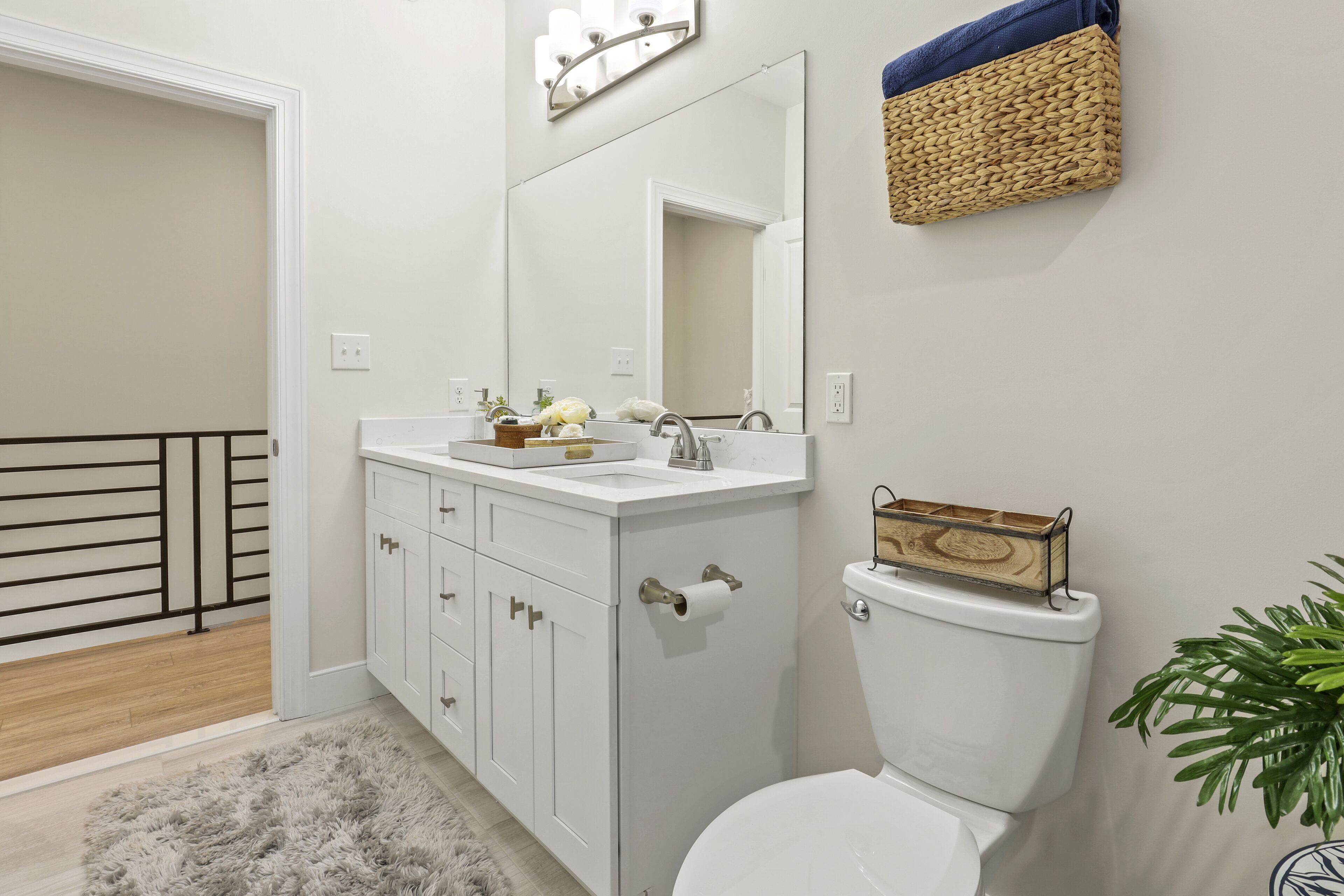 A bathroom with a white sink, mirror, and toilet. There is a wooden basket on the wall and a plant next to the toilet.