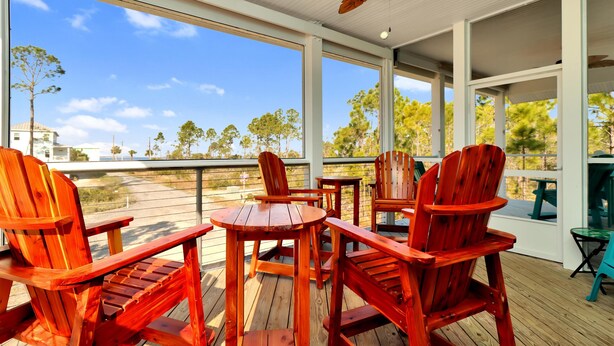 A covered outdoor area with wooden chairs and tables, large windows offering a view of the beach and palm trees. - Dolphin Daze (Port St. Joe)