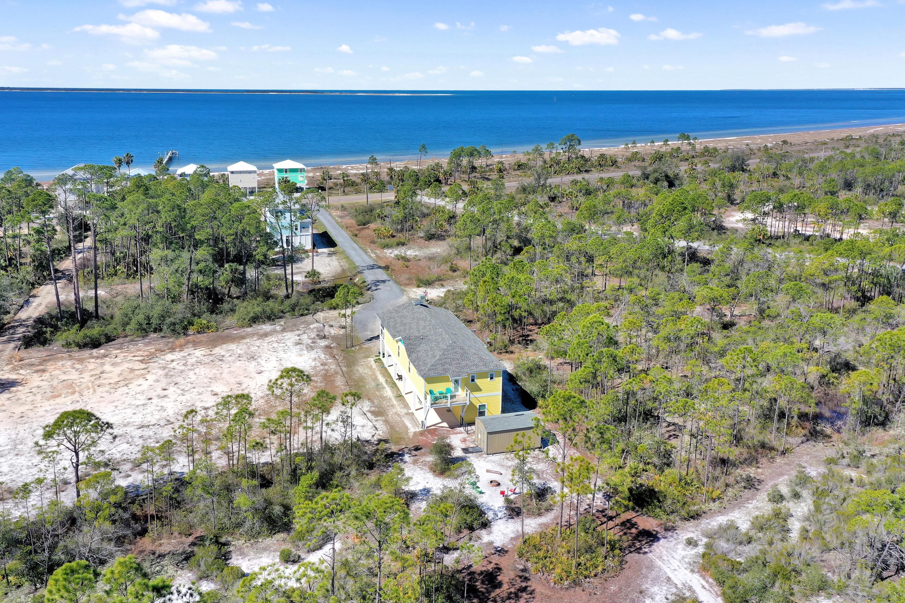 An aerial view of a coastal property with a main building, a beach, and a forested area.