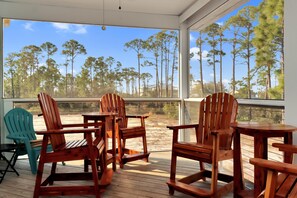 A wooden deck with chairs and a table, overlooking a forested area.