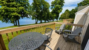 Een houten terras met een ronde tafel en stoelen, met uitzicht op water en bomen.
