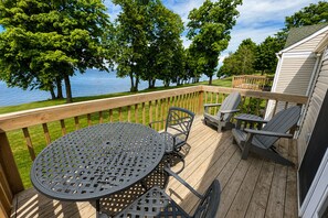 A wooden deck with a round table and chairs, overlooking a body of water and trees.