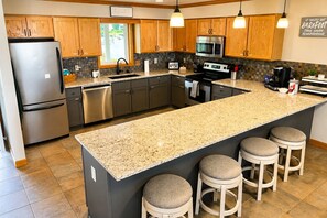 A modern kitchen with wooden cabinets, stainless steel appliances, a granite countertop, and bar stools.