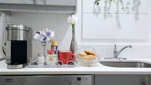 Une cuisine avec une machine à café, un vase rempli de fleurs, une tasse rouge et un bol de biscuits.