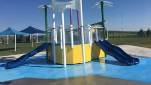 Une aire de jeux avec un toboggan jaune et bleu, une structure d’escalade et une balançoire.