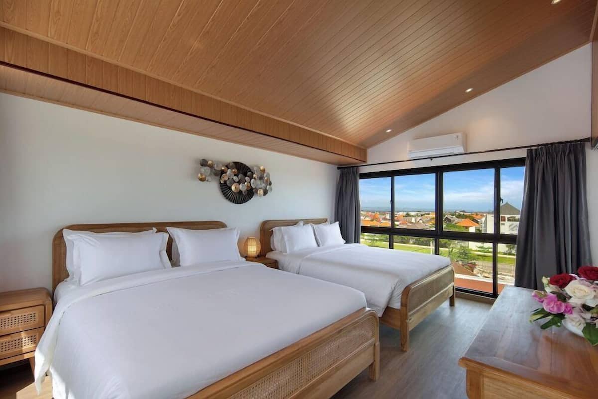 Une chambre d’hôtel avec deux lits, une grande fenêtre donnant sur la ville, un plafond en bois et un climatiseur fixé au mur.