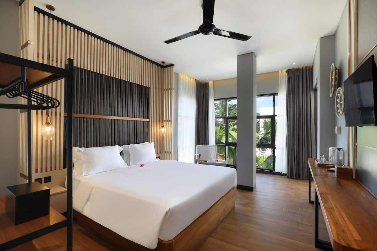 Une chambre d’hôtel moderne dotée d’un grand lit, d’un ventilateur de plafond, d’un bureau en bois et offrant une vue sur l’extérieur.