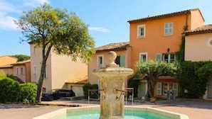 A square stone fountain with a central spout and water flowing into a basin, surrounded by a paved area with buildings in the background. - House for 4 people with air conditioning in a private domain with a pool located in Gassin (GASSIN)