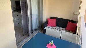 A balcony with a blue table, a wicker sofa with red cushions, and a sliding glass door. - Studio in Pin Rolland, beach and shops on foot (ST MANDRIER SUR MER)